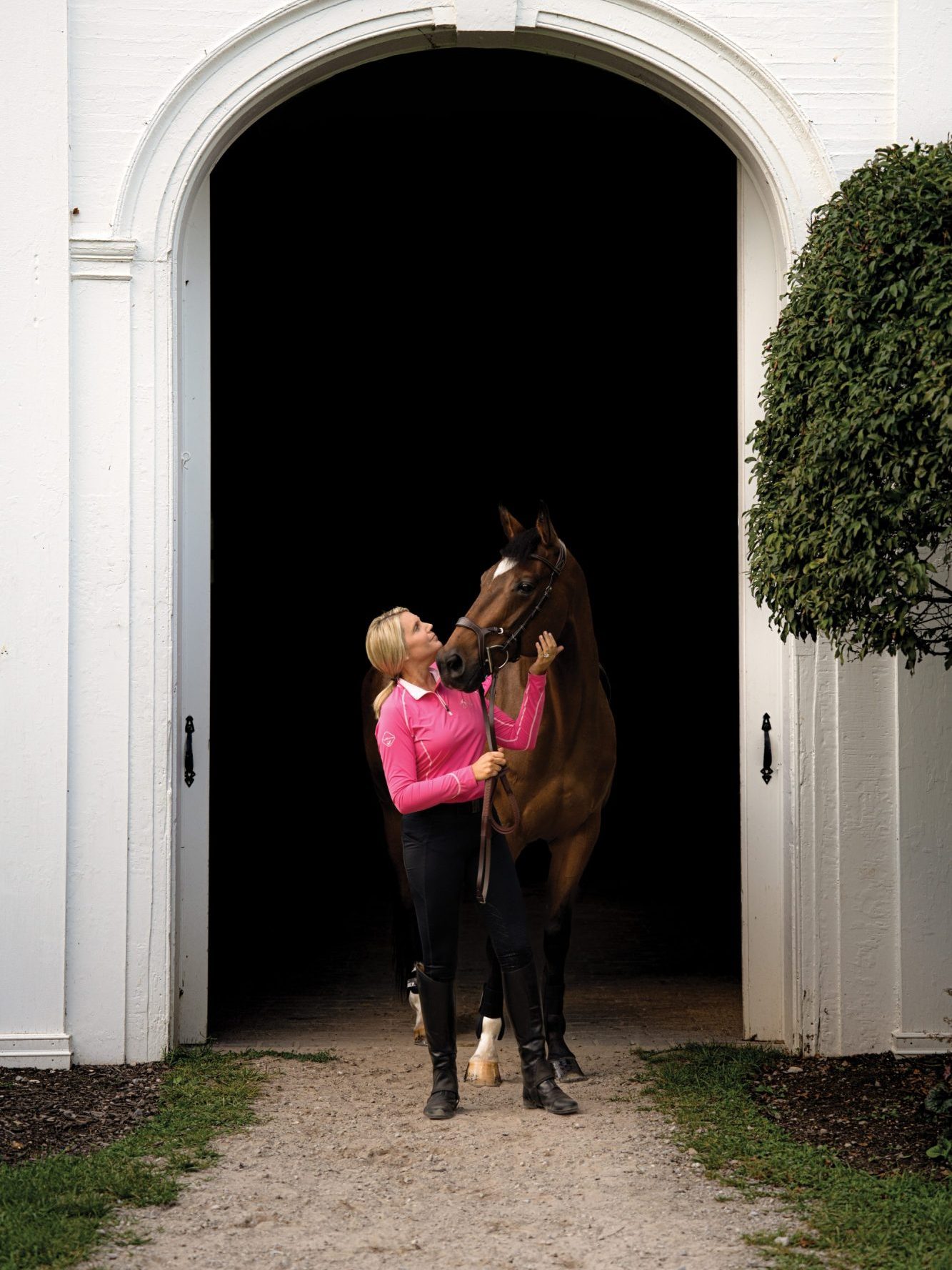 Horse rider pets her bay horses cheek while they look at each other during a lifestyle product shoot at a stable.